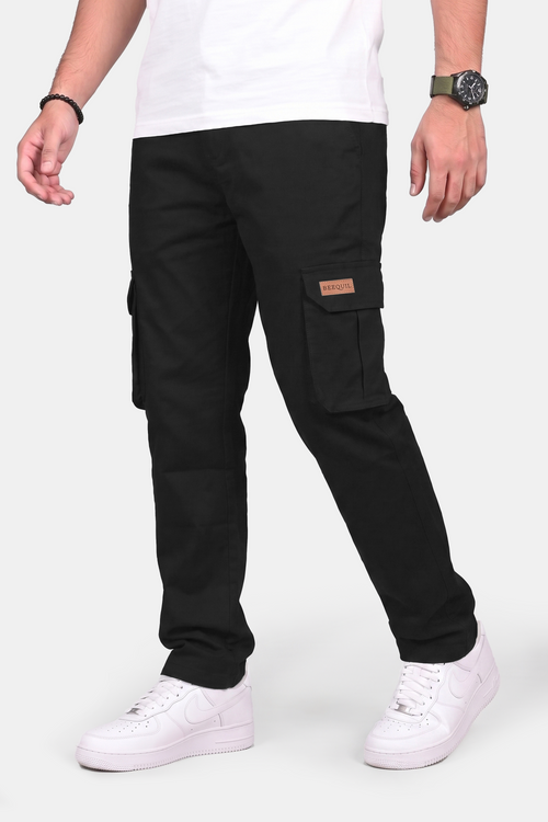 A person wearing black cargo pants with side flap pockets, a white t-shirt, and white sneakers, shown from the waist down against a light gray studio background.