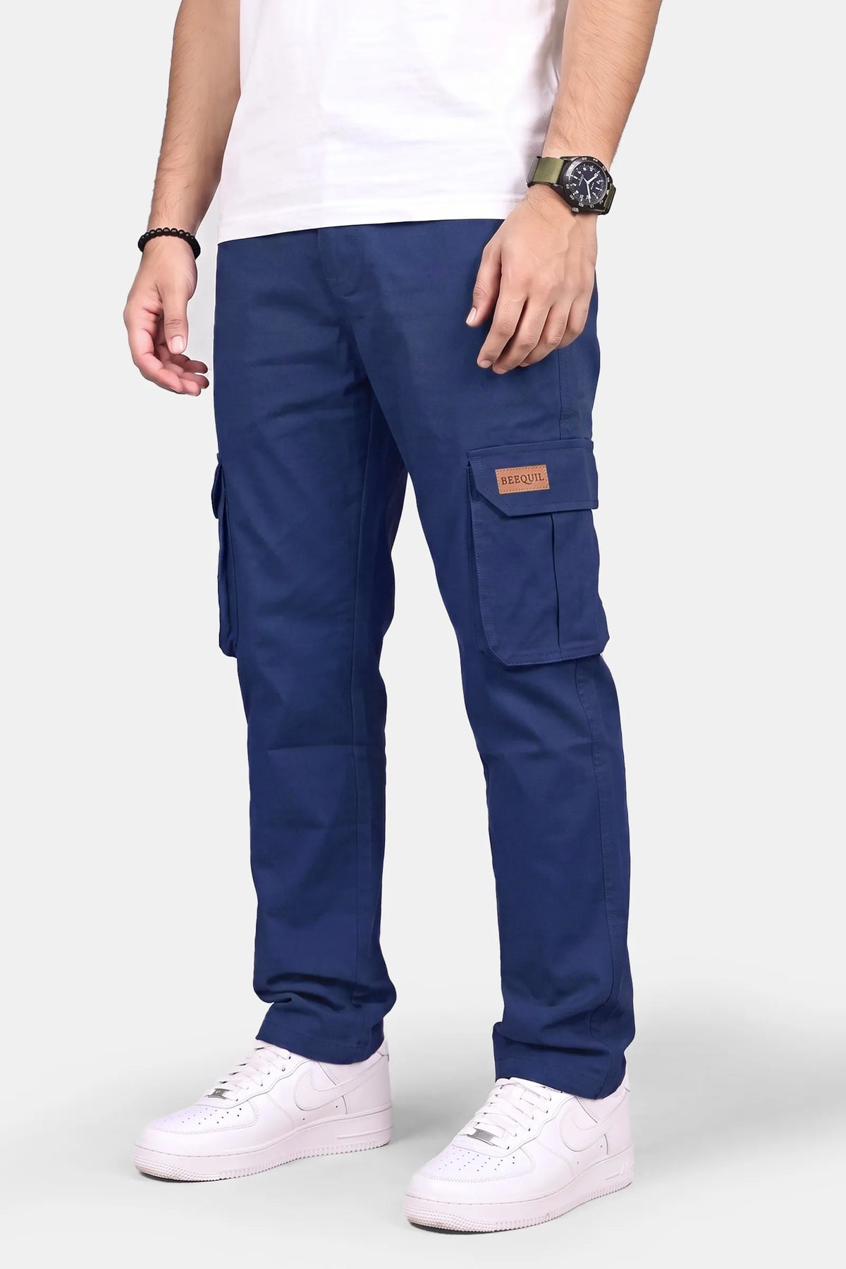 A person wearing navy blue cargo pants with white sneakers and a white t-shirt, shown from the waist down against a light gray studio background.