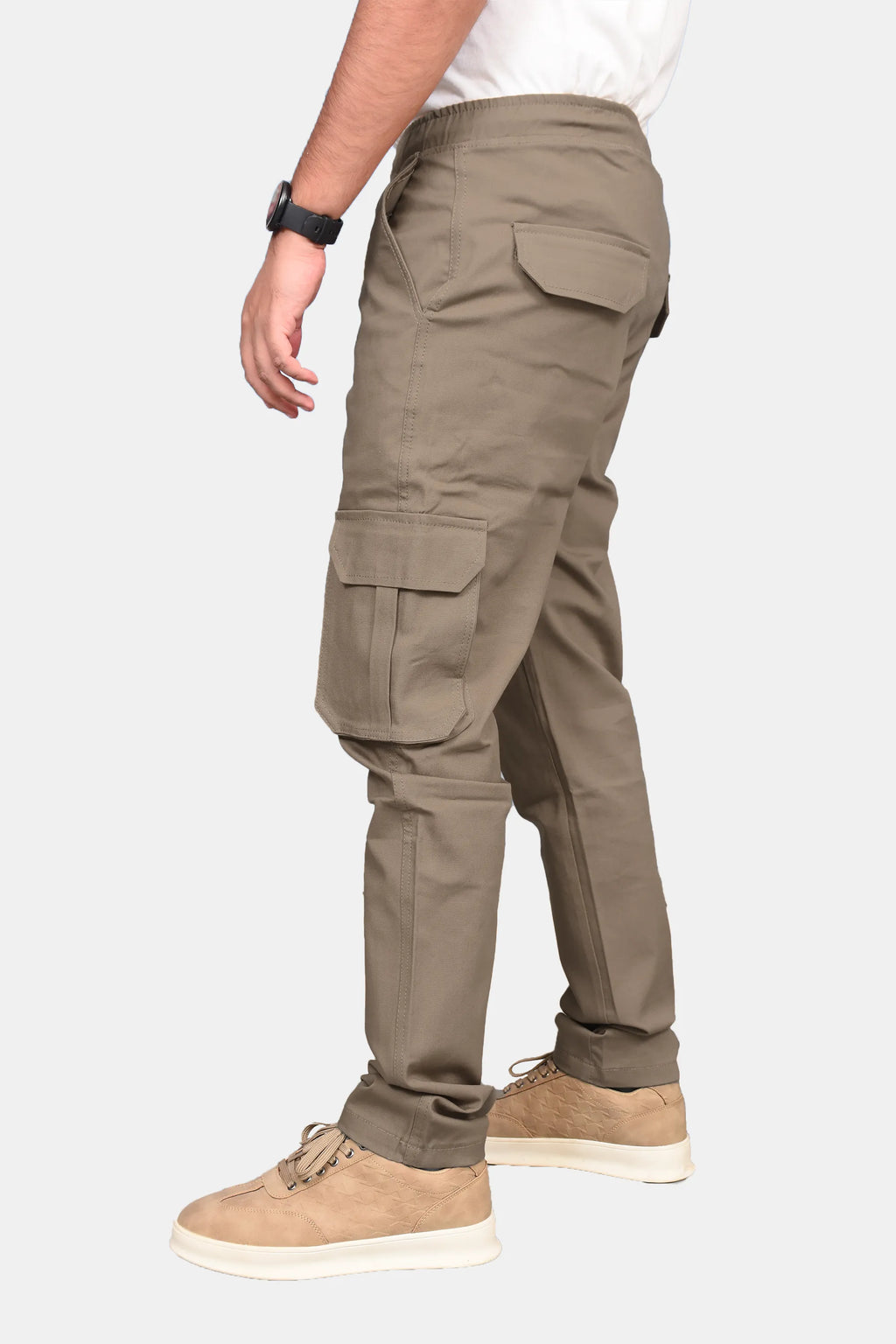 A side profile view of a person wearing khaki cargo pants, a white t-shirt, and tan suede sneakers against a light gray background.