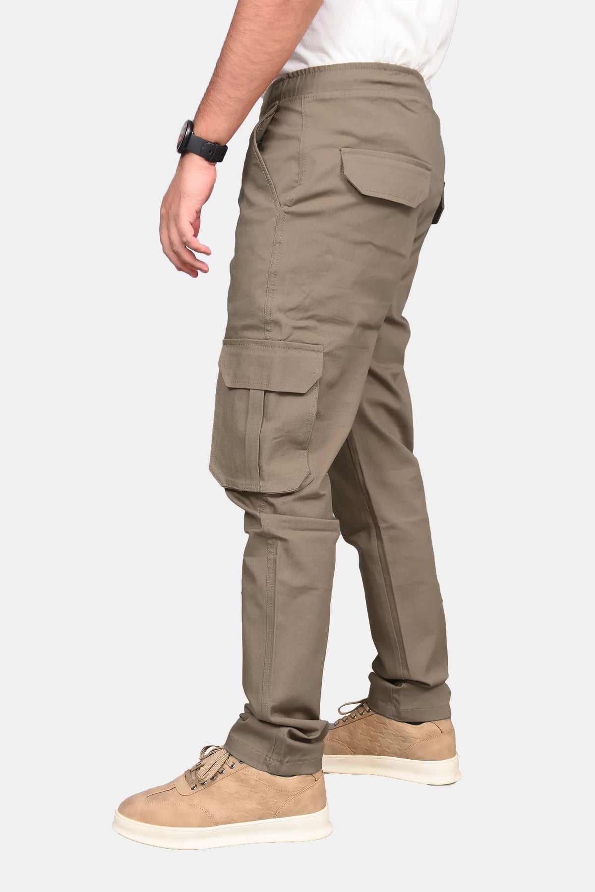 A side profile view of a person wearing khaki cargo pants, a white t-shirt, and tan suede sneakers against a light gray background.