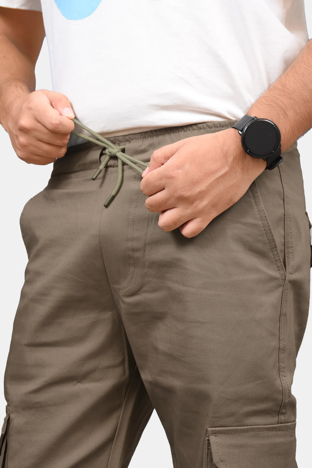 A close-up of a person wearing desert brick cargo pants, pulling the drawstring at the waistband. The person is also wearing a white t-shirt and a black smartwatch.