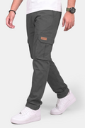A person wearing dark gray cargo pants with a brown patch on the side pocket, styled with a white t-shirt and white sneakers against a light gray background.