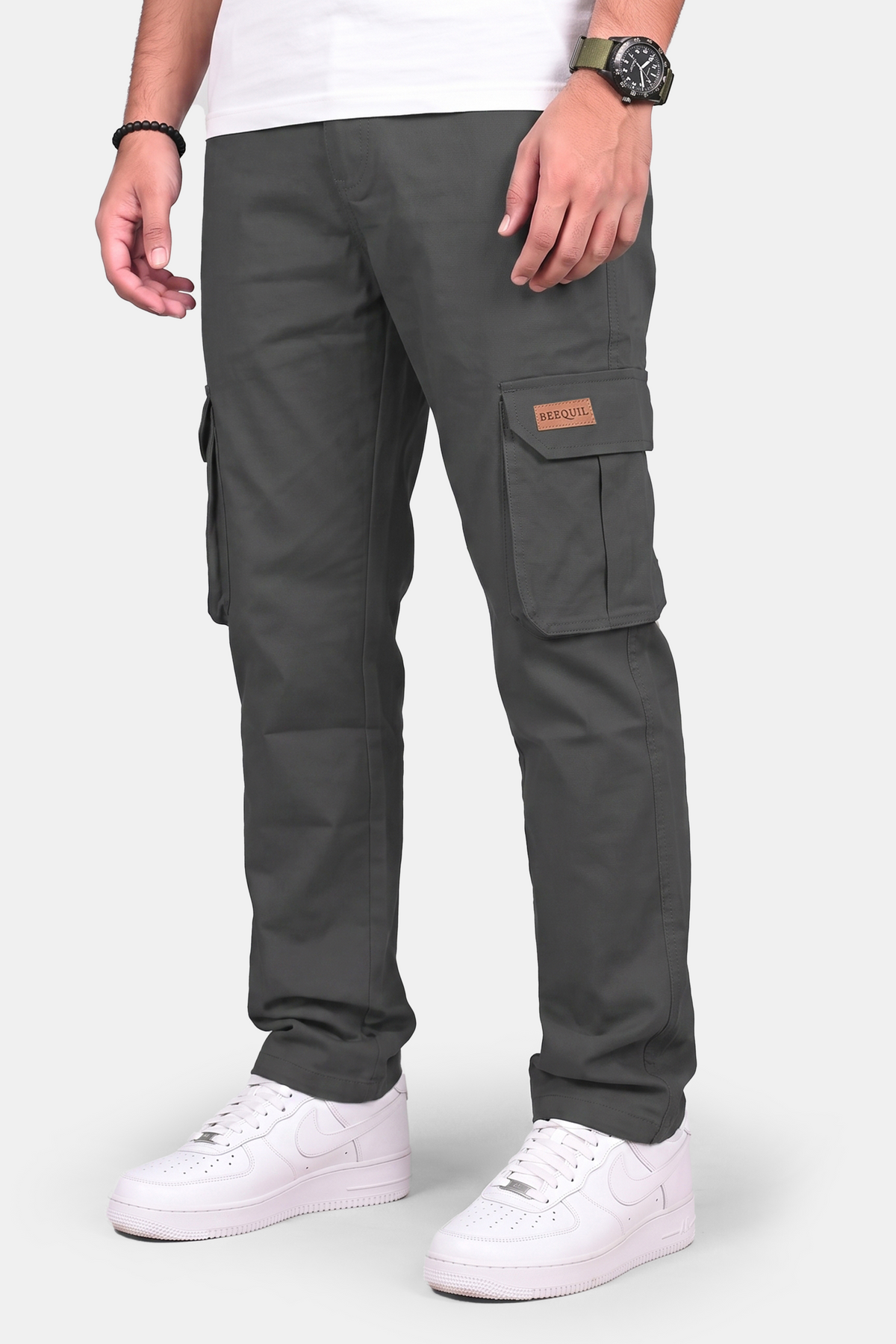 A person wearing dark gray cargo pants with white sneakers and a white t-shirt, shown from the waist down against a light gray studio background.