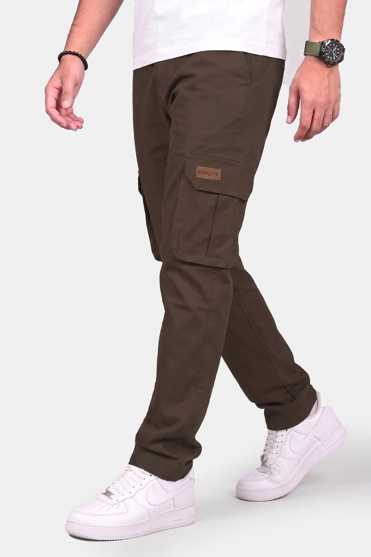 A person wearing dark brown cargo pants with white sneakers and a white t-shirt, shown from the waist down against a light gray background.